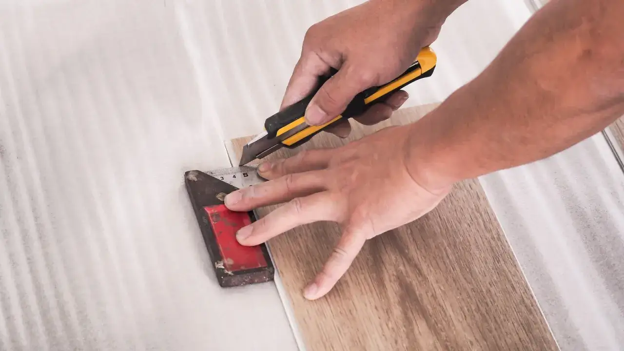 Hands using a utility knife and a metal ruler to score LVT flooring. This shows how to cut LVT flooring for a perfect fit.