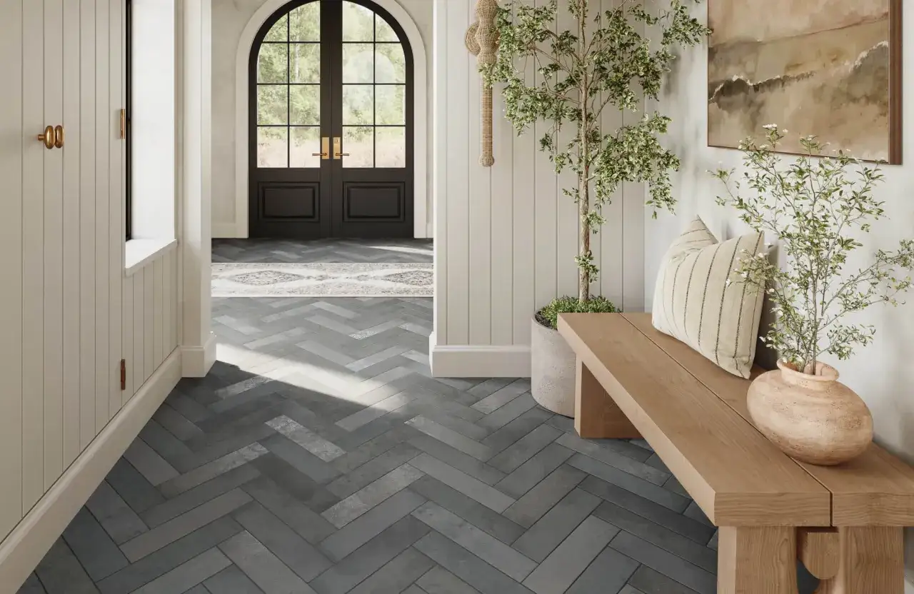 A modern entryway with a herringbone pattern of dark subway tile on the floor, leading to double doors.