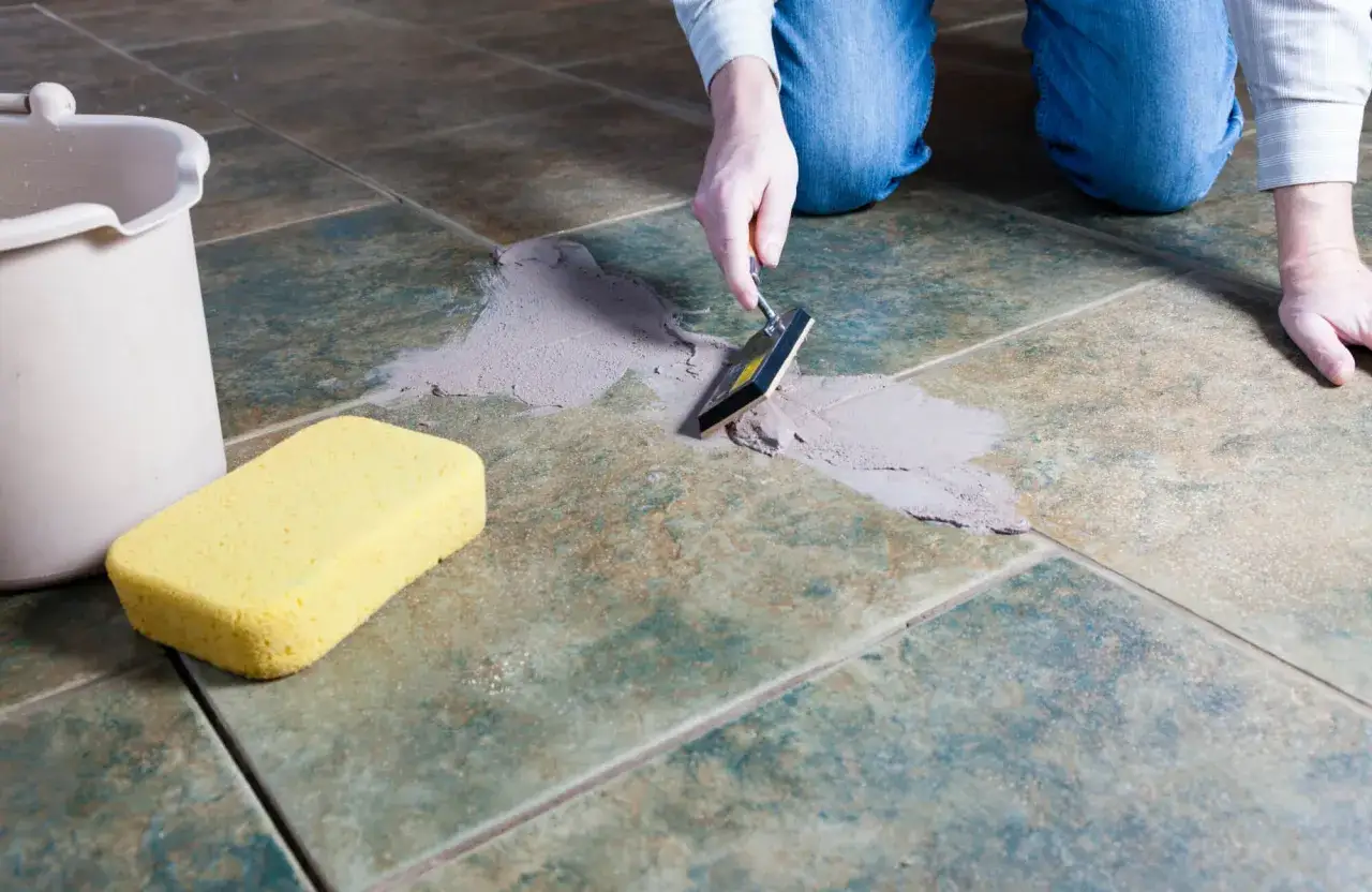 Applying grout to tile seams with a trowel. A sponge and bucket are nearby, ready for cleaning up after learning how to grout subway tile.