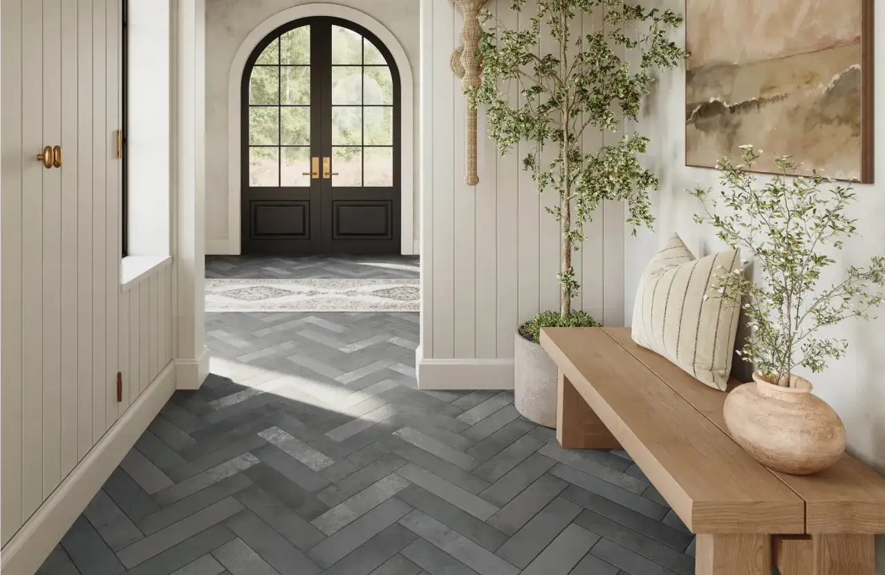 Herringbone tile direction creates an illusion of a larger space in this entryway, featuring a wooden bench, potted plant, and arched double doors.