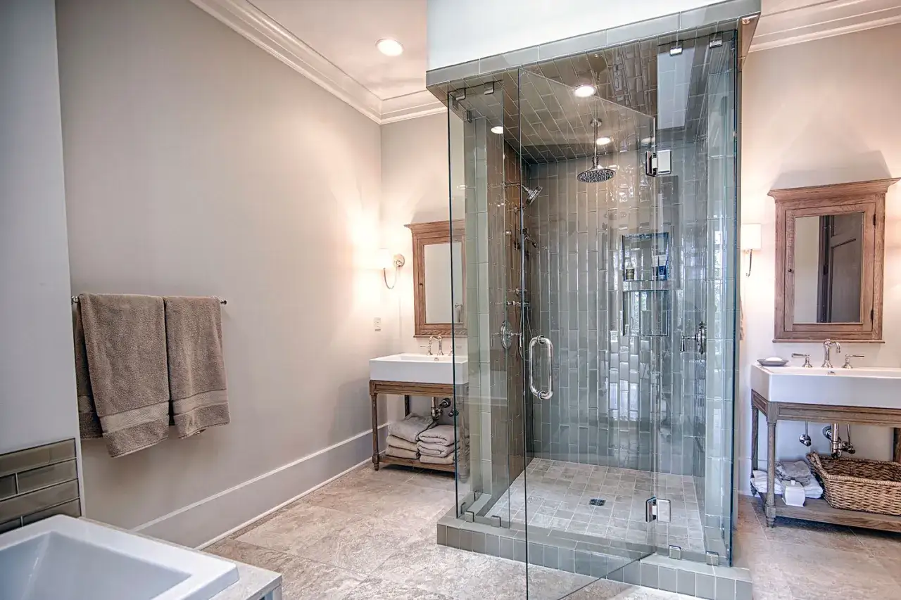 A modern bathroom with a glass-enclosed shower, dual sinks, and elegant natural stone flooring.