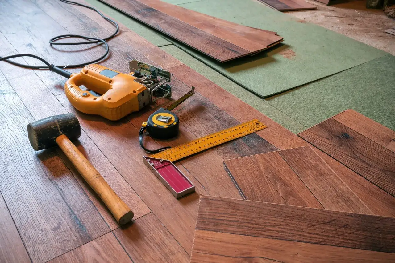 Tools for how to cut flooring: jigsaw, rubber mallet, tape measure, and a square on wood planks.