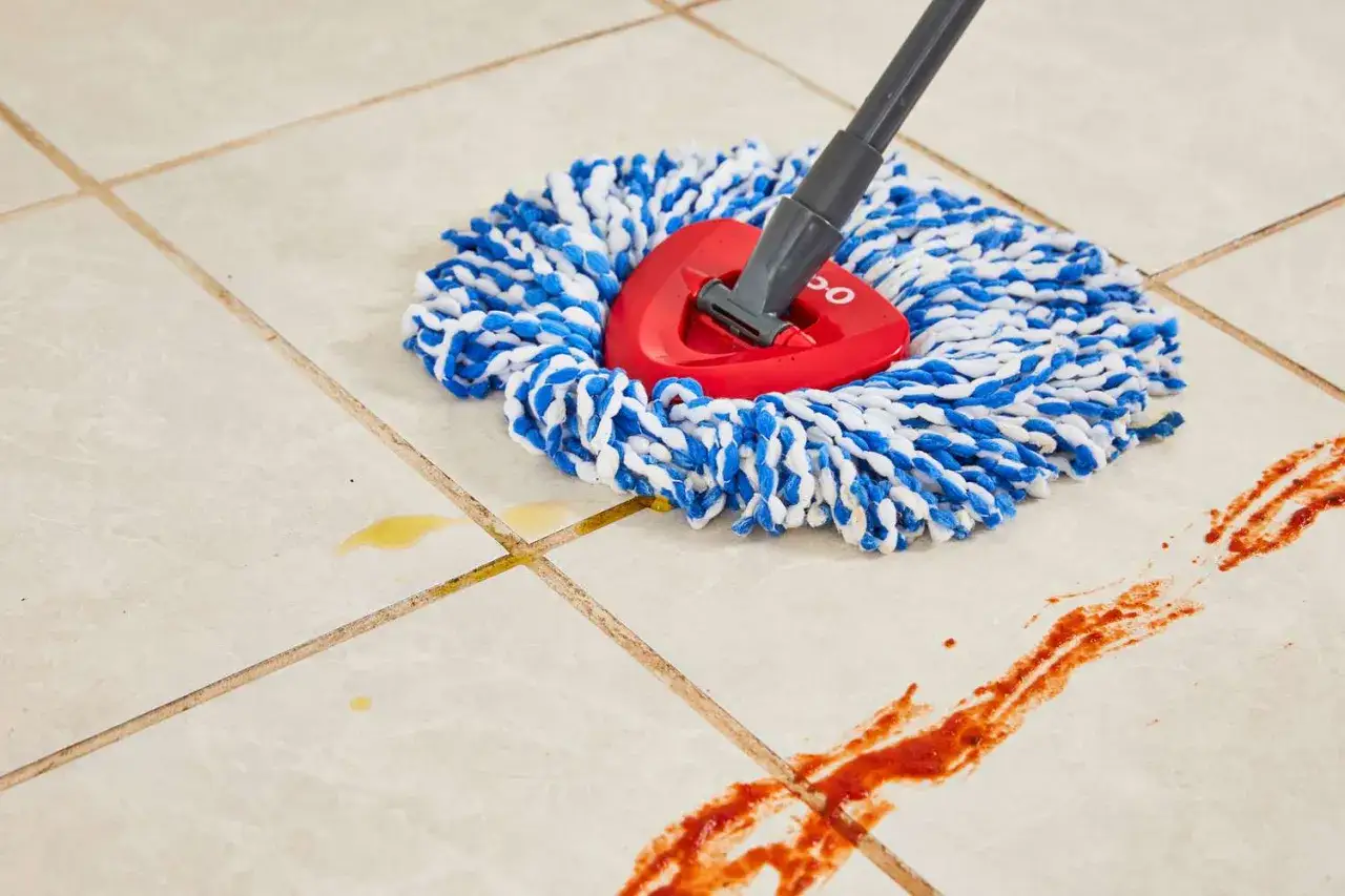 A mop with blue and white strands is cleaning up spills on beige porcelain tile, showing the best way to clean porcelain tile.