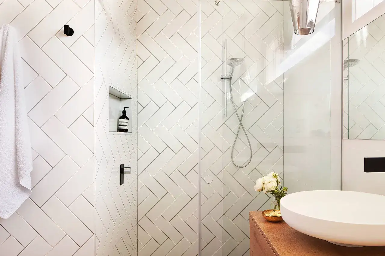 A modern bathroom with white chevron tile walls, a glass shower enclosure, and a white vessel sink. Chevron tile is timeless, not out of style!