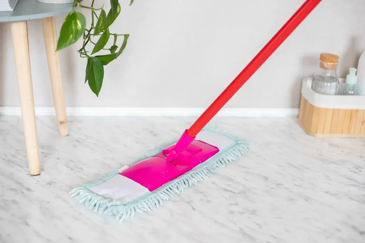 A bright pink mop head with a red handle is cleaning a shiny marble floor.