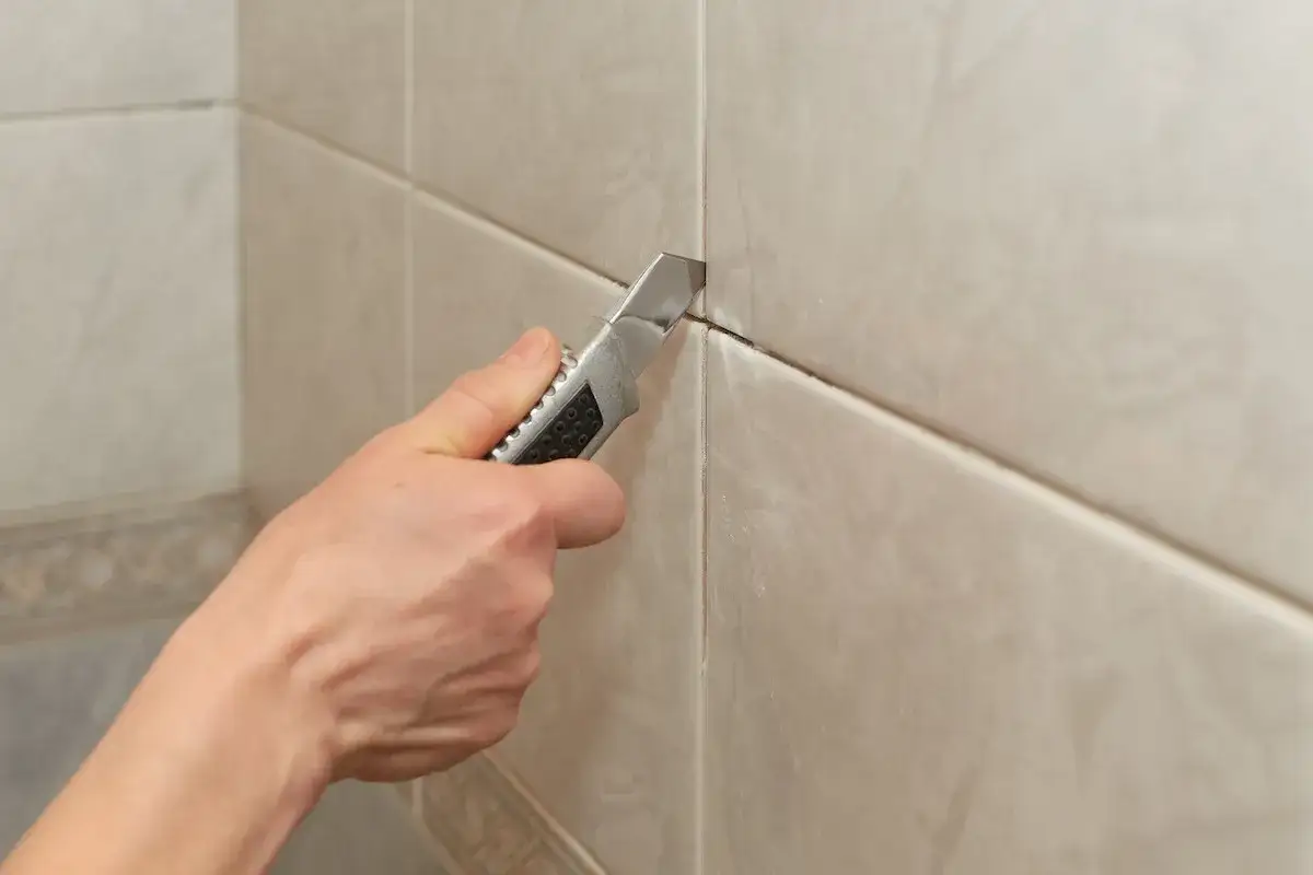 Removing old grout with a utility knife is the first step to the best way to regrout tiles.