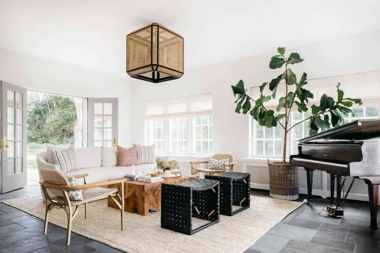 A bright living room with a white sofa, a wooden coffee table, and a piano. Dark floors are present, but the room feels spacious, not smaller.