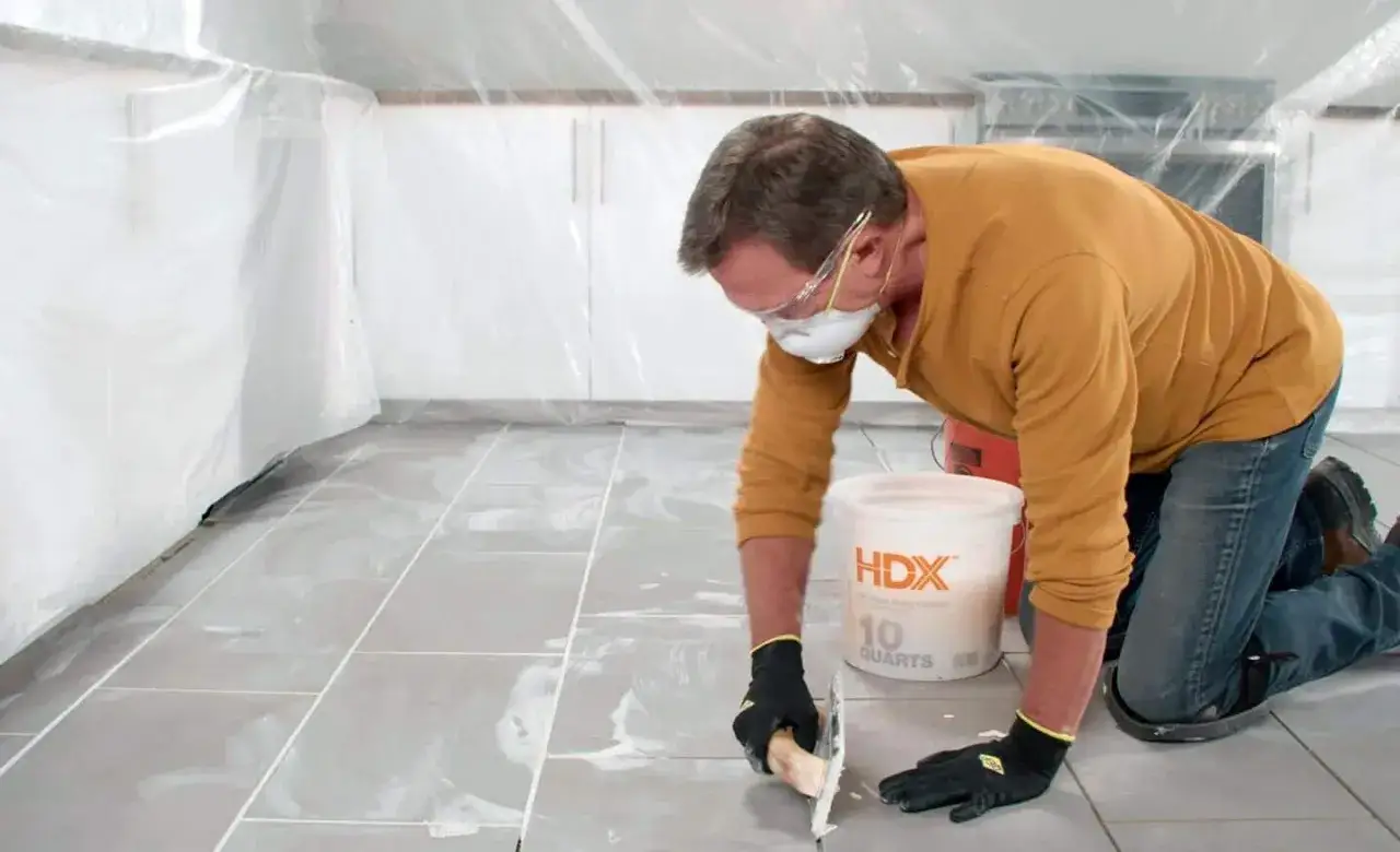 Man in protective gear carefully repairing grouting on a tiled floor.