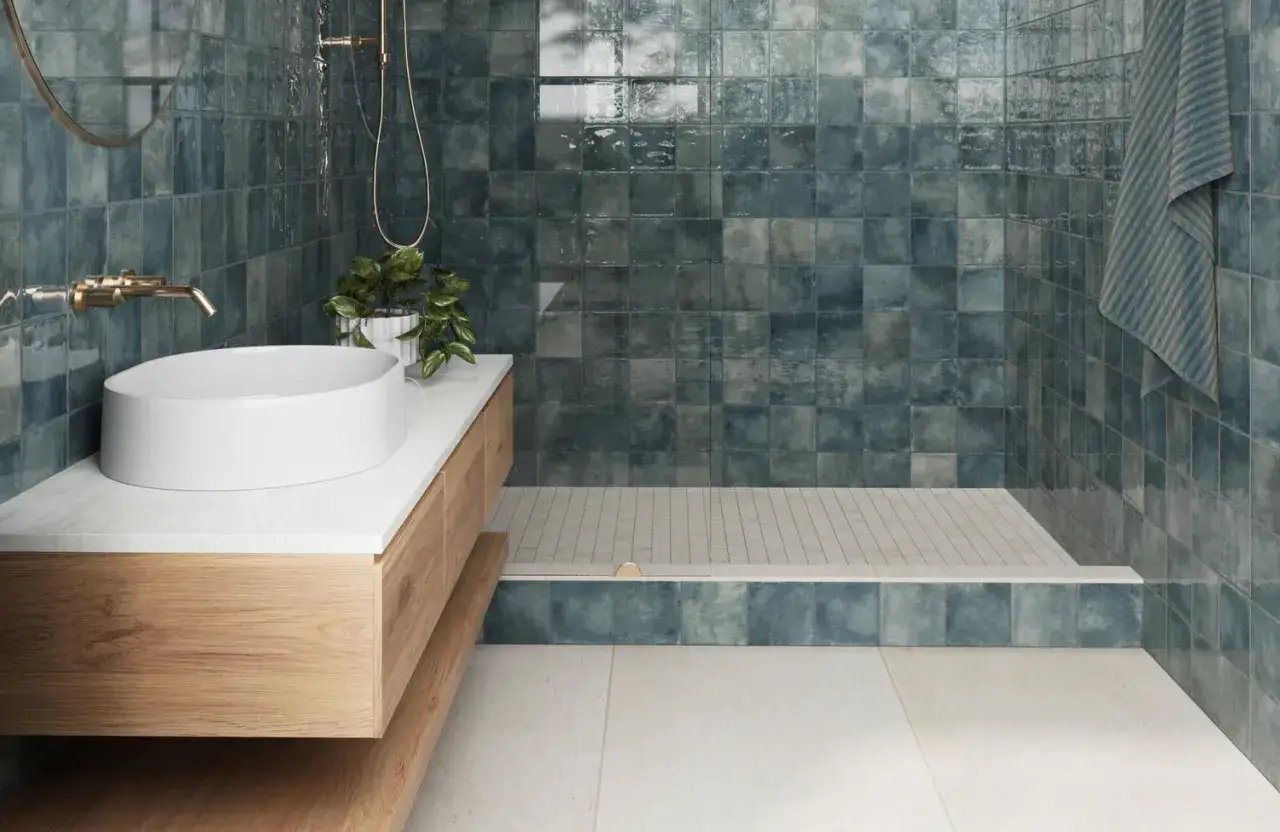 A modern bathroom with a floating vanity, vessel sink, and a shower tiled in deep blue squares. This shows what bathroom tile is made of.