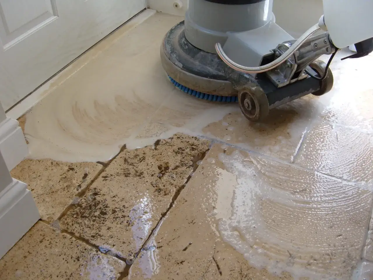 A floor buffer is used to clean travertine tile, creating suds and removing dirt.
