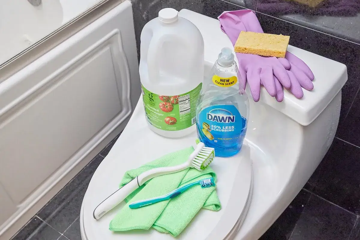 Gather supplies for how to clean toilet tank: vinegar, dish soap, gloves, sponge, microfiber cloths, and brushes.