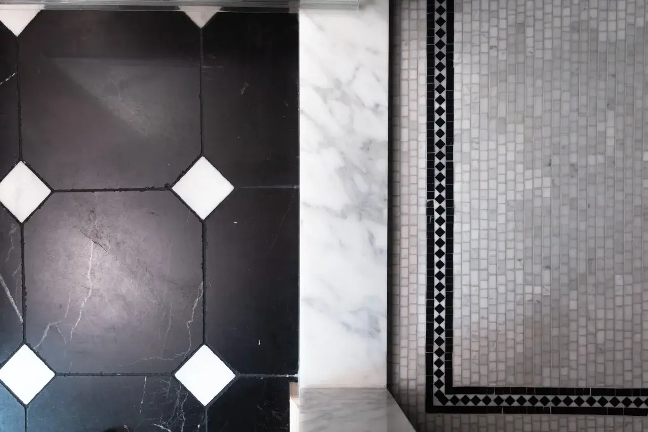 A striking floor design featuring large black marble tiles with white accents and black grout, next to a mosaic of small white marble tiles bordered by a black diamond pattern.
