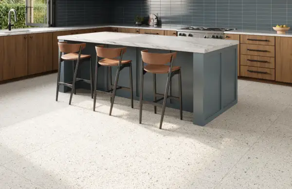 A modern kitchen with a blue island, wooden cabinets, and a beautiful bella terrazzo floor. Three bar stools are pulled up to the island.