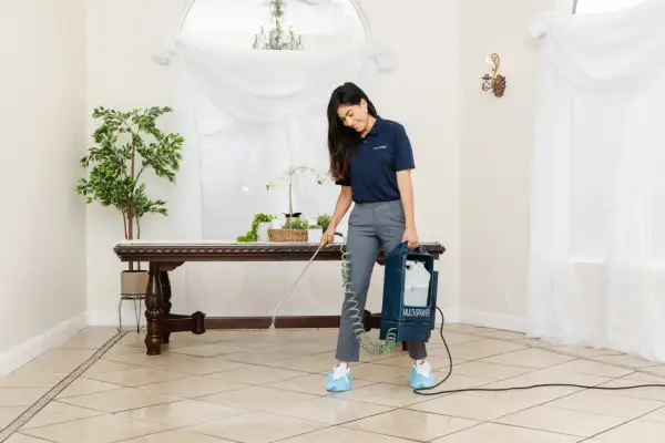 A woman uses a multi-sprayer for polished porcelain tile cleaner, ensuring a spotless shine in a well-lit room with elegant decor.