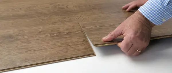 Hands demonstrate how to replace vinyl plank flooring by clicking a new plank into place.