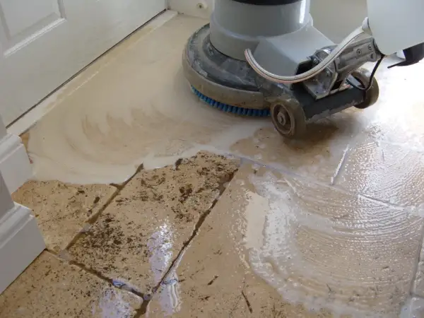 A floor buffer machine is used to clean travertine tile, creating suds and removing dirt.