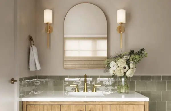 Elegant bathroom vanity with brass fixtures, a large arched mirror, and wall sconces that cast light up and down. A bouquet of white flowers adds a touch of luxury.