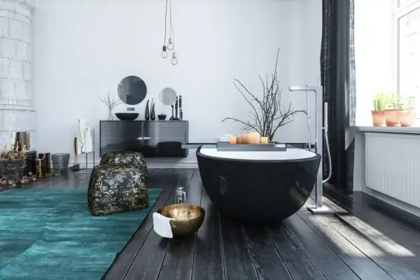 Modern bathroom with a black freestanding tub, dark wood floors, and a teal rug.
