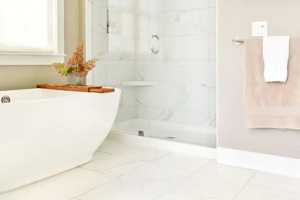 A modern bathroom with white marble tiles and a subtle marble tile grout color. A freestanding tub and glass shower create a spa-like feel.