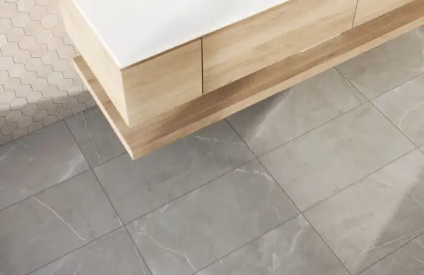 A modern bathroom vanity with wood grain drawers sits above large format tile flooring. The grout lines are thin, emphasizing the size of the tiles.