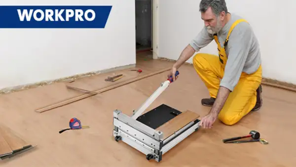 Man in yellow overalls uses a WORKPRO flooring cutter to demonstrate how to cut flooring. Tools and planks are nearby.
