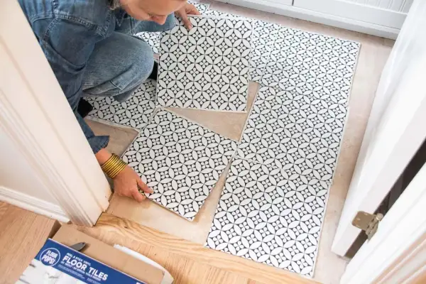 A person is laying down black and white patterned peel and stick floor tiles. No grout is needed for these tiles.