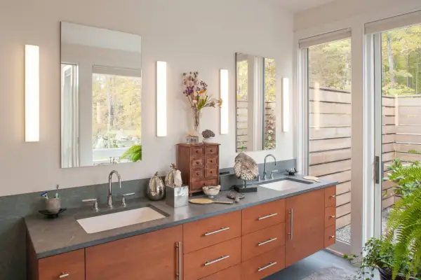 Modern bathroom vanity with two vertical lights over the sinks, reflecting a serene forest view.