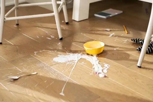 A yellow bowl has spilled white liquid and fruit on a laminate floor. Learn how to clean laminate floors effectively after such messes.