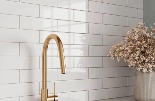 A gold faucet and dried flowers complement a white subway tile backsplash, showcasing a clean look after learning how to grout subway tile.