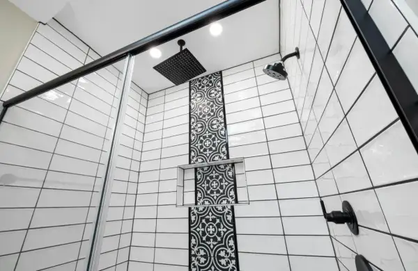 Modern shower with white subway tiles and black grout, featuring a decorative black tile accent and black fixtures.