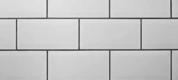 A clean, modern wall features rows of white tile with thin, dark grey grout lines, creating a classic subway tile pattern.