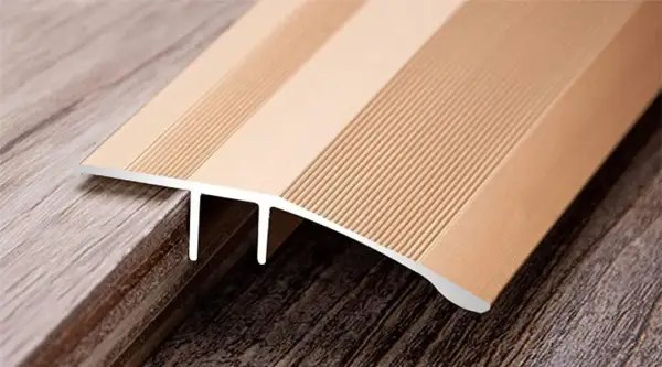 A metallic transition strip bridges two different wood-look floors, one lighter and one darker, showcasing the seamless finish of cut vinyl flooring.