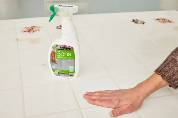 A hand wipes a stained porcelain floor tile with Bona Hard-Surface Floor Cleaner, showcasing effective porcelain floor tile cleaners.