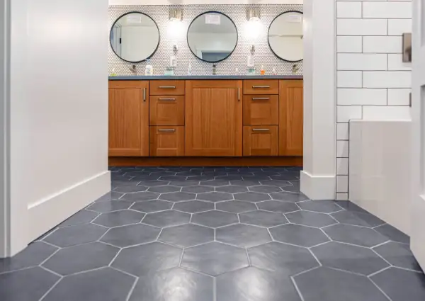 Hexagonal floor tiles create a dynamic pattern, giving the illusion of a larger space. A wooden vanity with three circular mirrors sits above.
