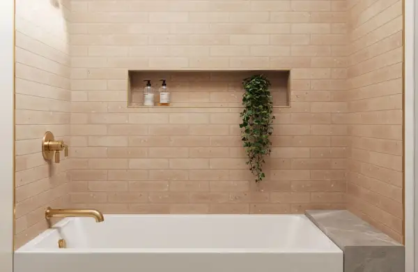 A modern bathroom with a random subway tile pattern in a warm, peachy hue. A gold faucet and shower controls complement the tiles.