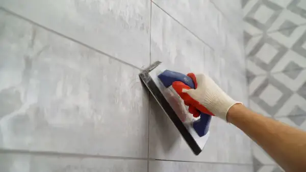 Gloved hand applies grout to a tiled wall, ensuring the best grout for shower floor longevity.