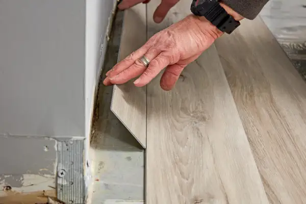 Hands installing light wood-look vinyl plank flooring. The question of how long does it take to install vinyl plank flooring depends on room size and prep.