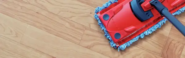 A red mop with blue fringe is cleaning a light wood-look vinyl floor, leaving it spotless.