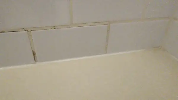 Cracked grout lines between light grey tiles suggest a need for repair. The question is, can you grout over grout?