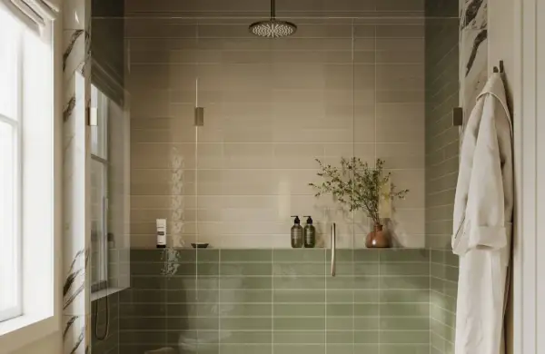 A modern shower with two-toned, low maintenance shower tile in beige and sage green. A glass enclosure, rainfall showerhead, and a plush robe complete the serene space.