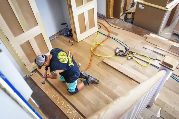 A worker applies adhesive to planks, demonstrating how to install luxury vinyl tile. Tools and materials are nearby.