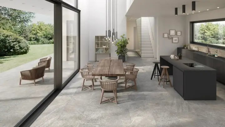 Modern dining and kitchen area with a seamless stone flooring installation, connecting indoor and outdoor spaces.